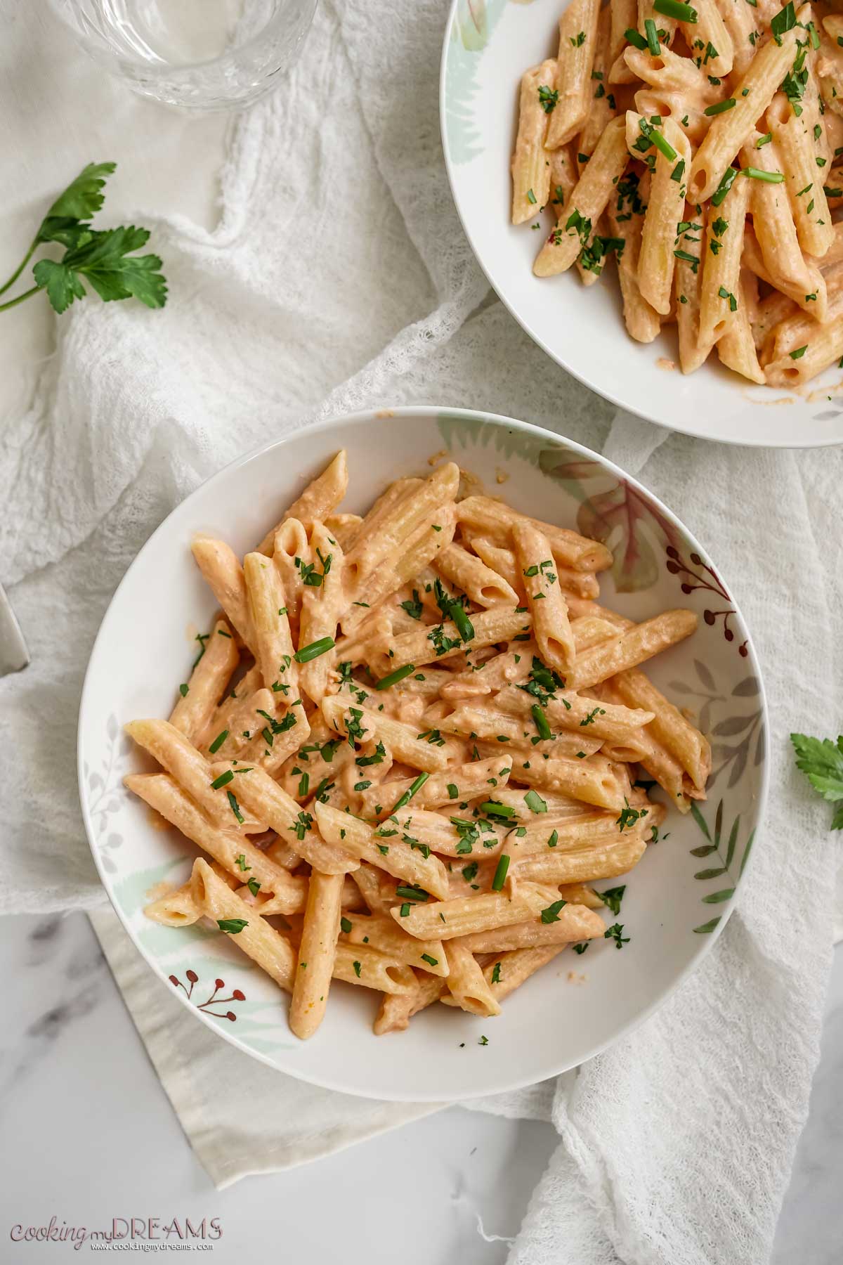 two dishes of penne al salmone topped with parsley.