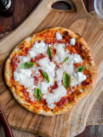 margherita pizza topped with basil on a wooden board.