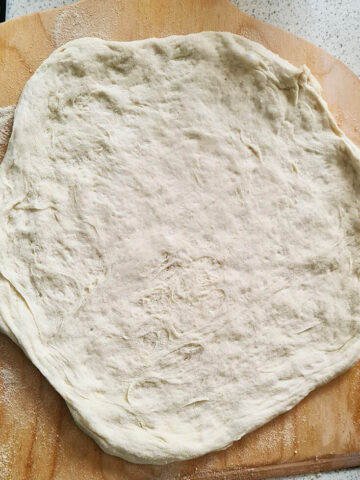 pizza dough shaped in a cirle on a wooden board.