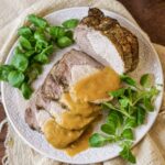 roast pork loin (arista) sliced and served on a platter with the gravy on top.