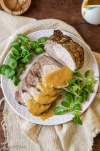 roast pork loin (arista) sliced and served on a platter with the gravy on top.