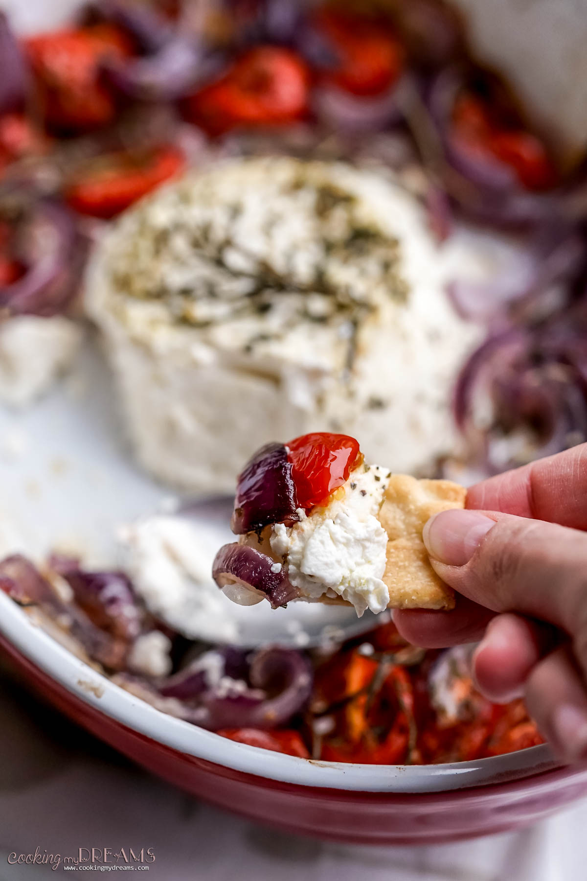 hand dipping a bite of baked ricotta and veggies with a cracker.