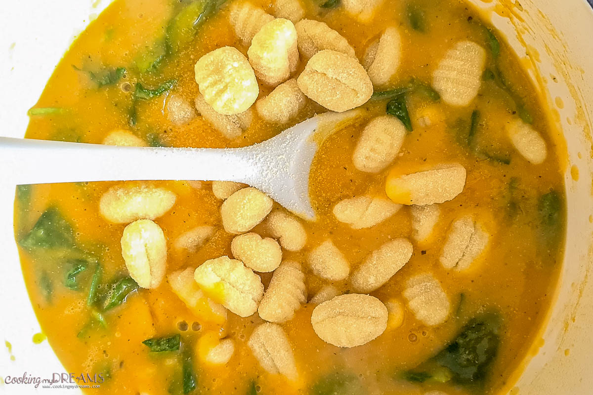 spoon mixing gnocchi and spinach into the pumpkin soup.