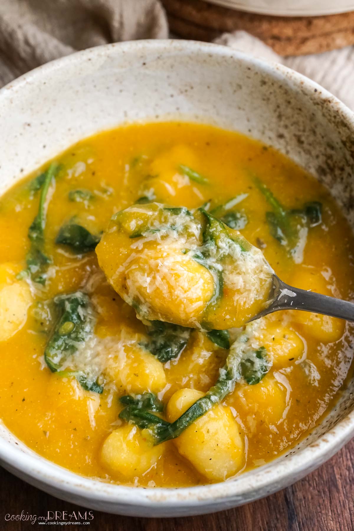 Spoon lifting pumpkin gnocchi soup with spinach.