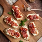 baked brie and prosciutto crostini on a wooden board.