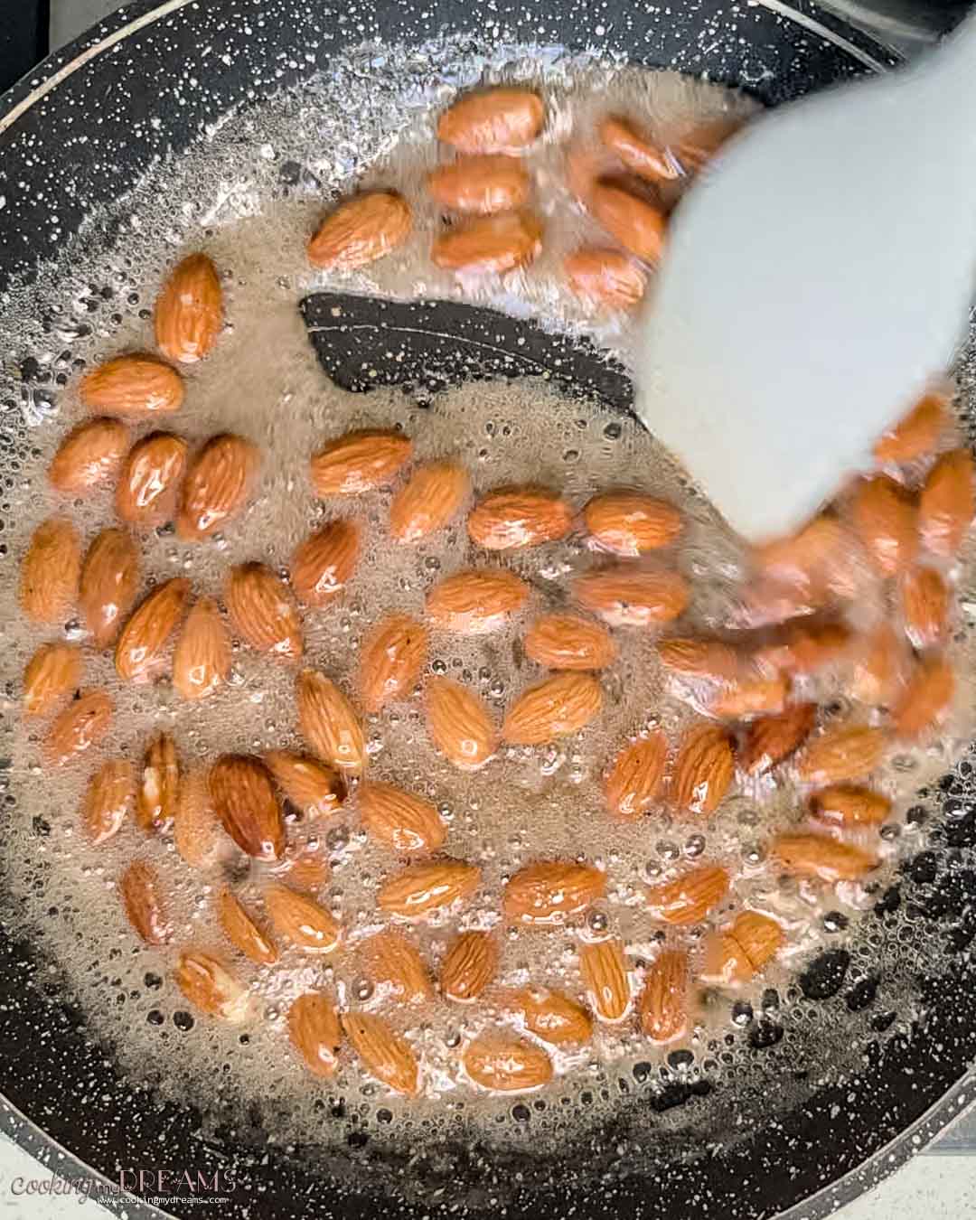 spatula stirring almonds in sugar syrup.