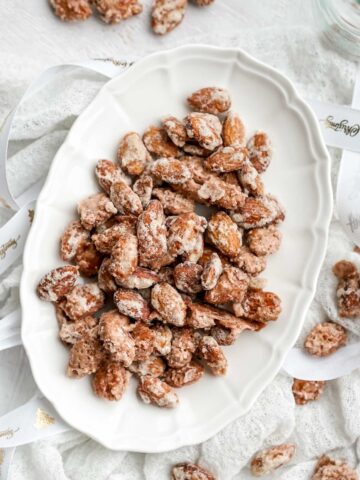 serving dish full of candied almonds on a white cloth.