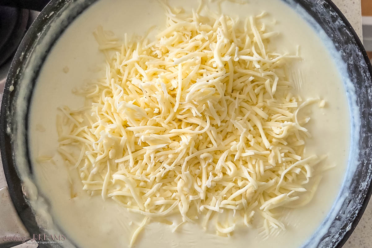 shredded cheese added to a pot of bechamel sauce.