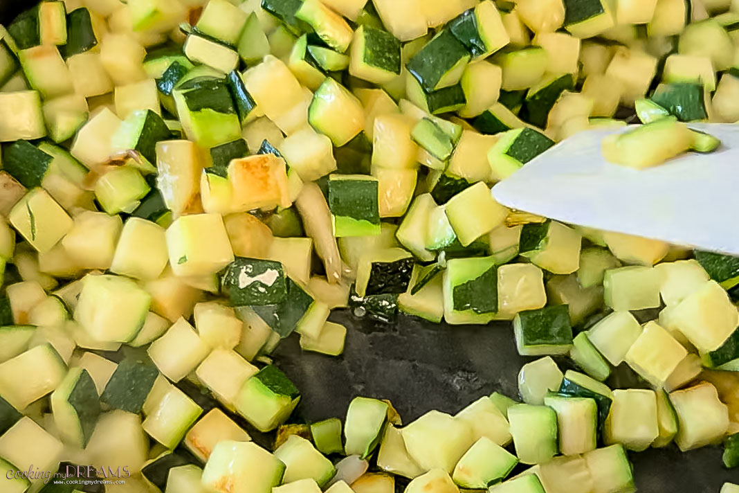 chopped zucchini sautèeing in a pan.