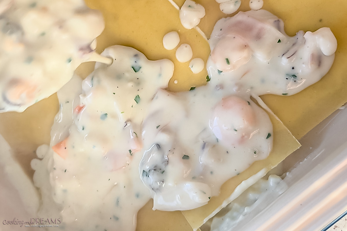 ladle spooning seafood sauce on a layer of lasagna sheets.