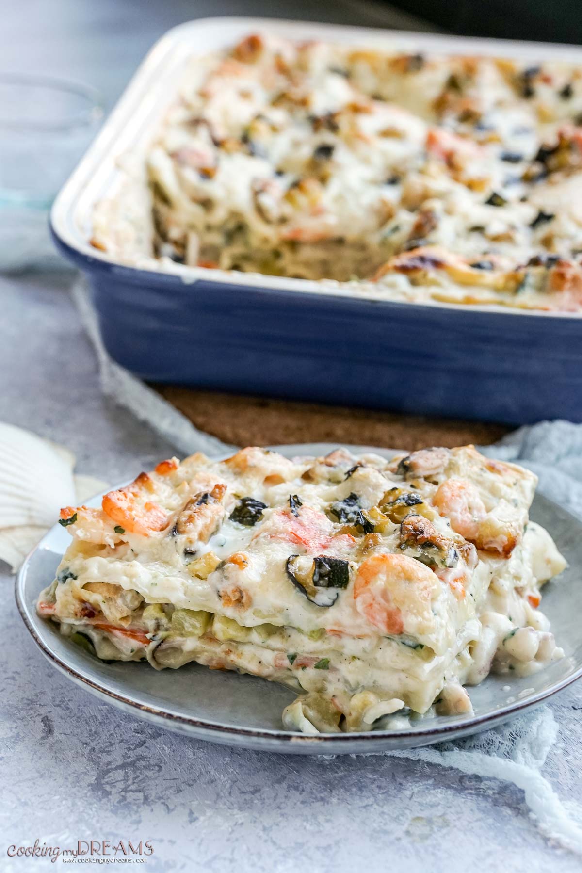 portion of seafood lasagna on a plate in front of the baking dish.