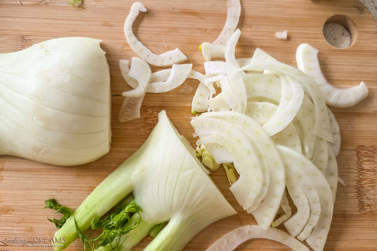 fennel bulb getting thinly sliced on a cutting board.