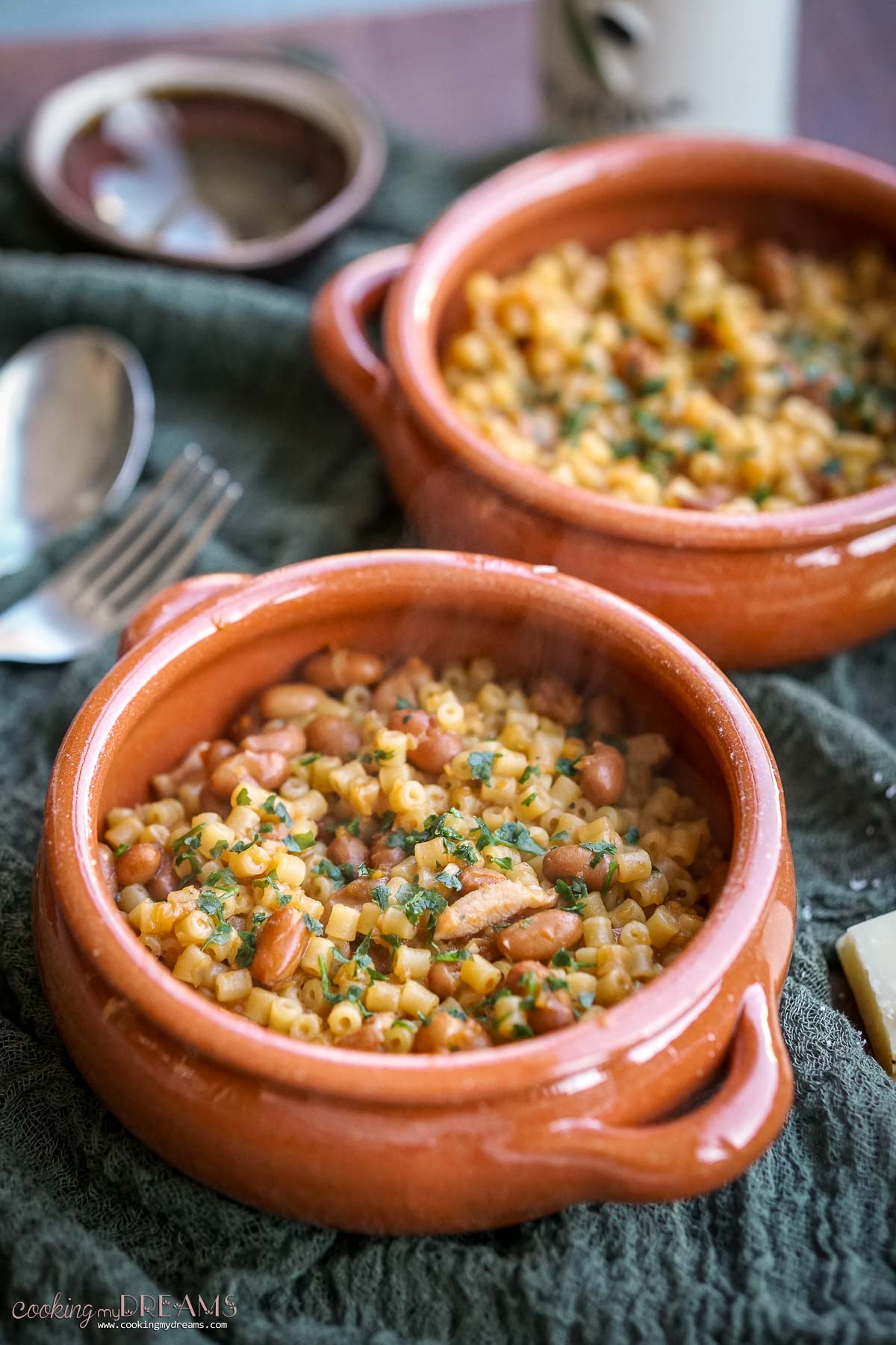 two terracotta bowls with pasta and beans on a green towel.