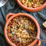 spoon inside a terracotta bowl of pasta and beans.