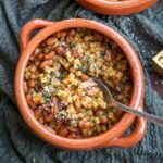spoon inside a terracotta bowl of pasta and beans.
