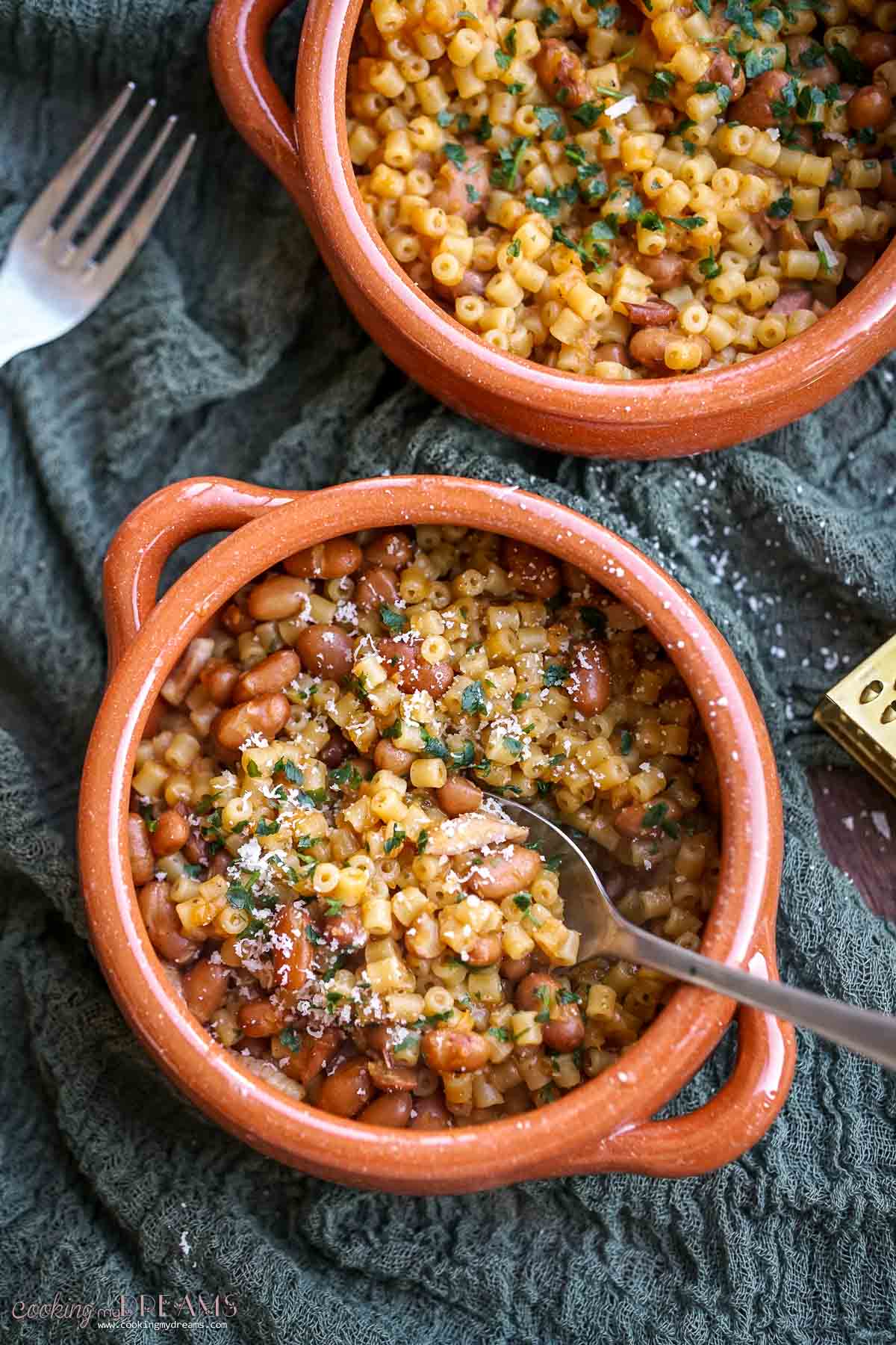 spoon inside a terracotta bowl of pasta and beans.