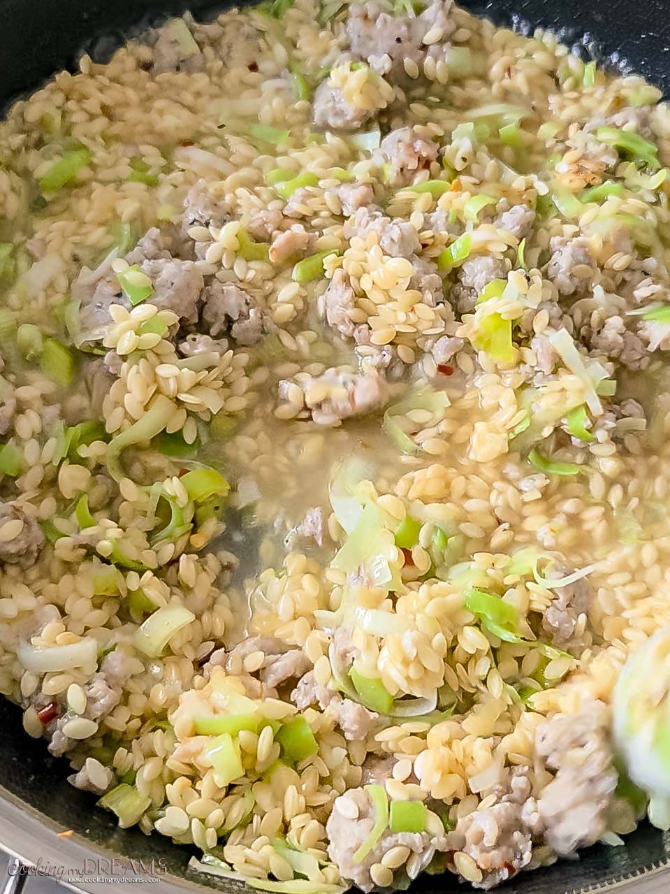 orzo is added to the skillet and covered with broth.