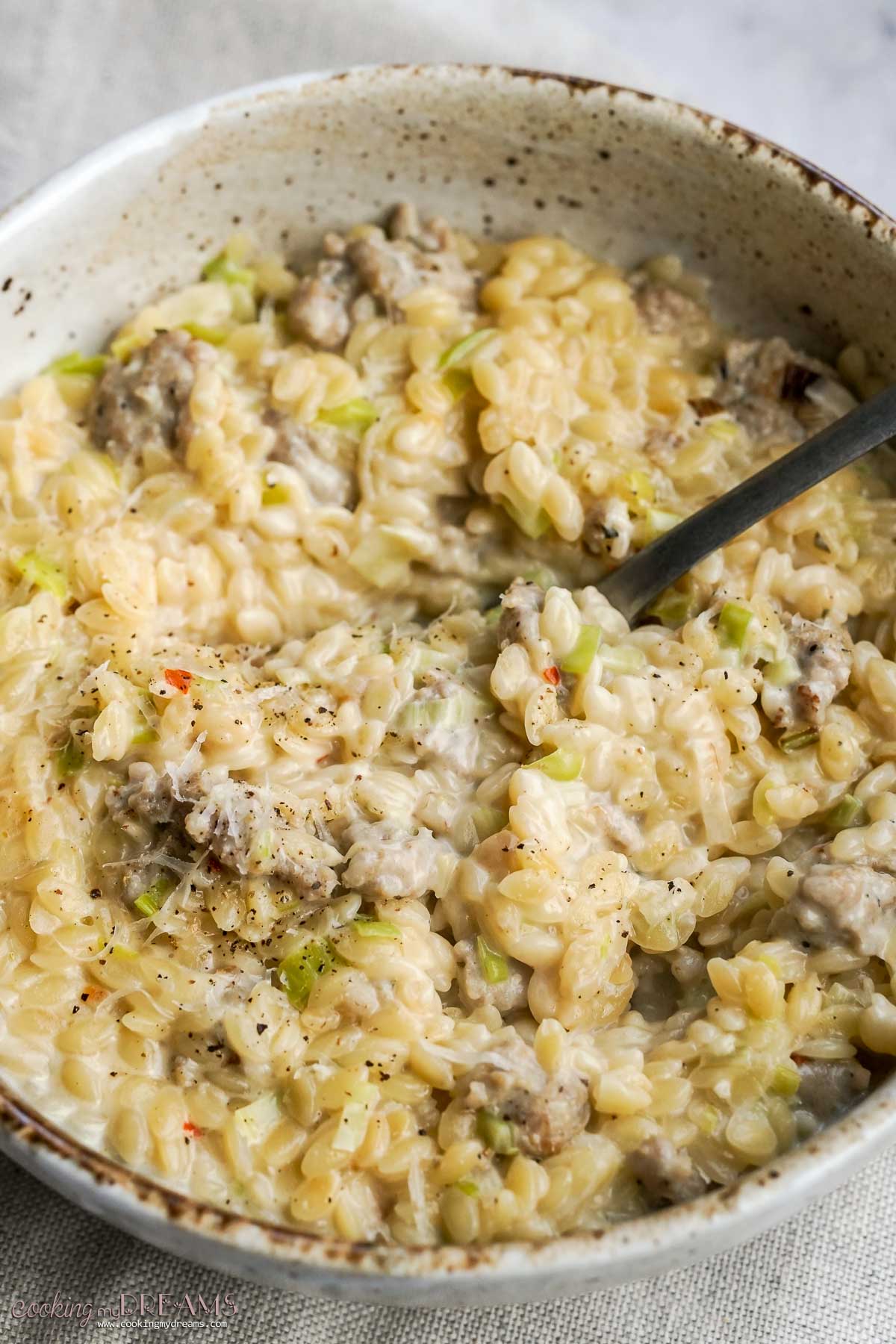 spoon inside a bowl with sausage leek orzo.