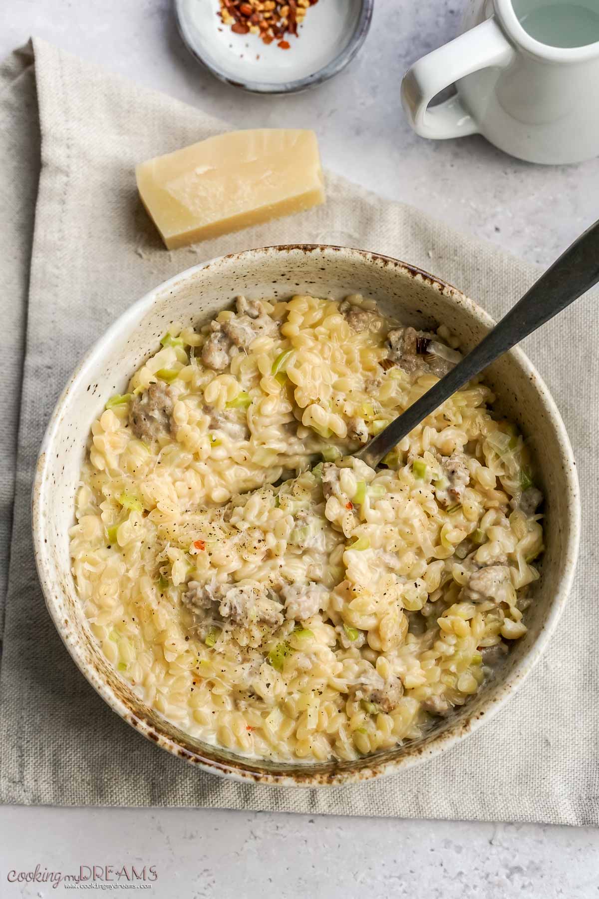 bowl with sausage and leek orzo on top of a towel with a spoon inside.