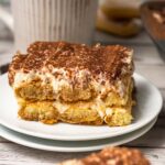 a portion of tiramisu on a plate next to the full tray.