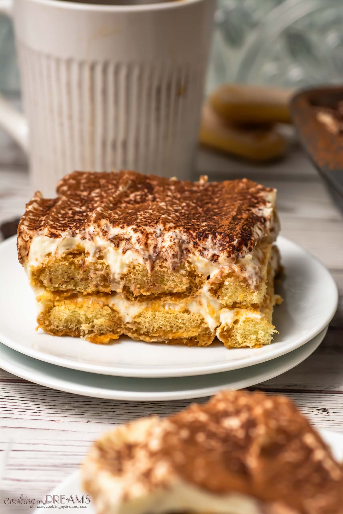 a portion of tiramisu on a plate next to the full tray.