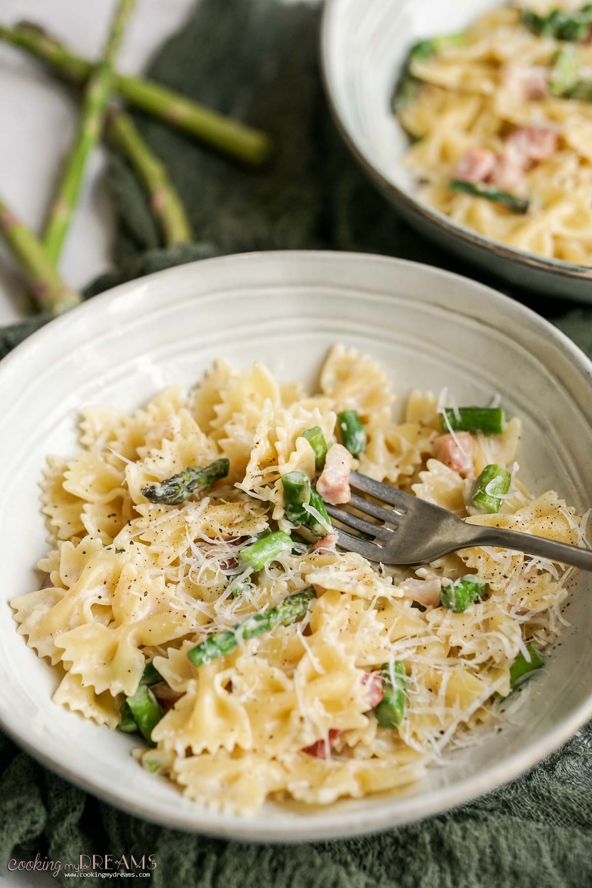 fork taking a bite of creamy pasta with aspragus and pancetta.