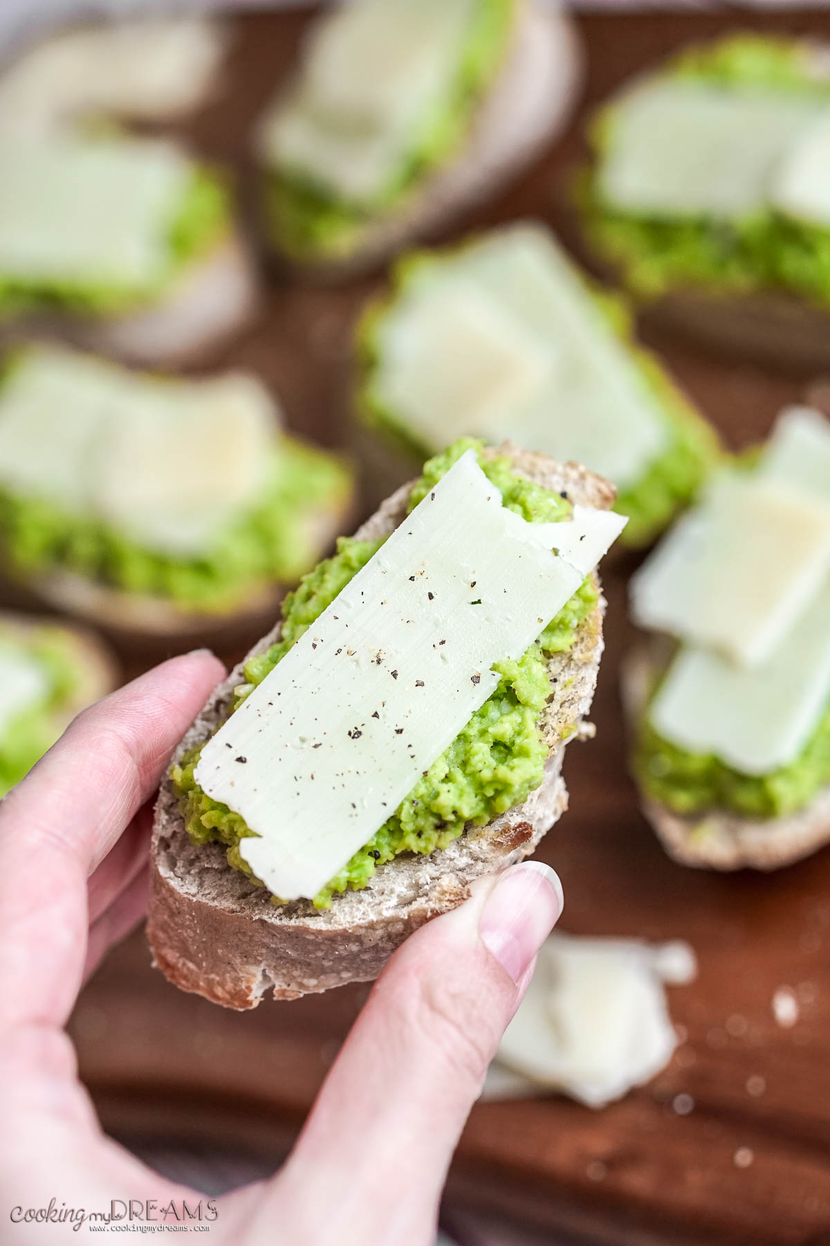 hand holding a fava and pecorino crostini.
