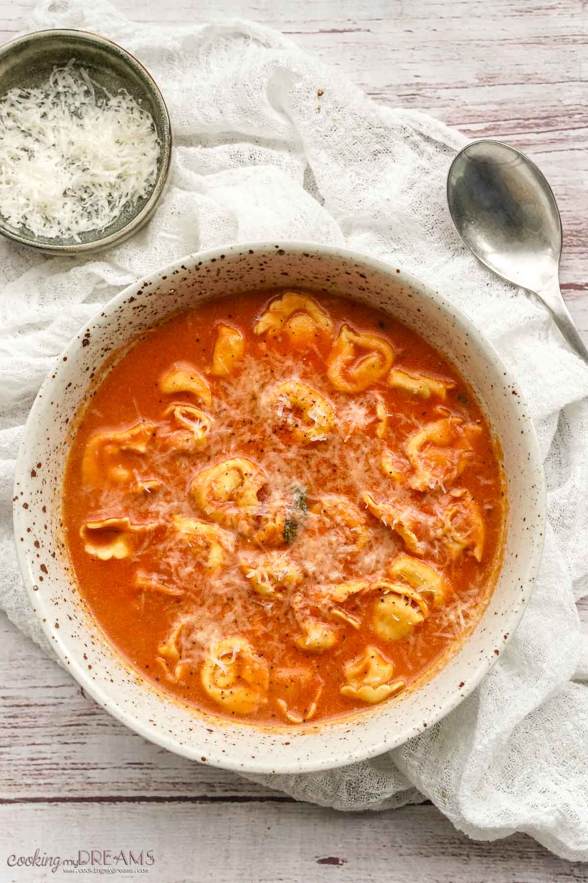 bowl of tomato tortellini soup on a white table.