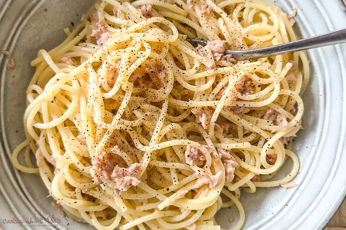 spaghetti with butter and tuna in a bowl with a fork.