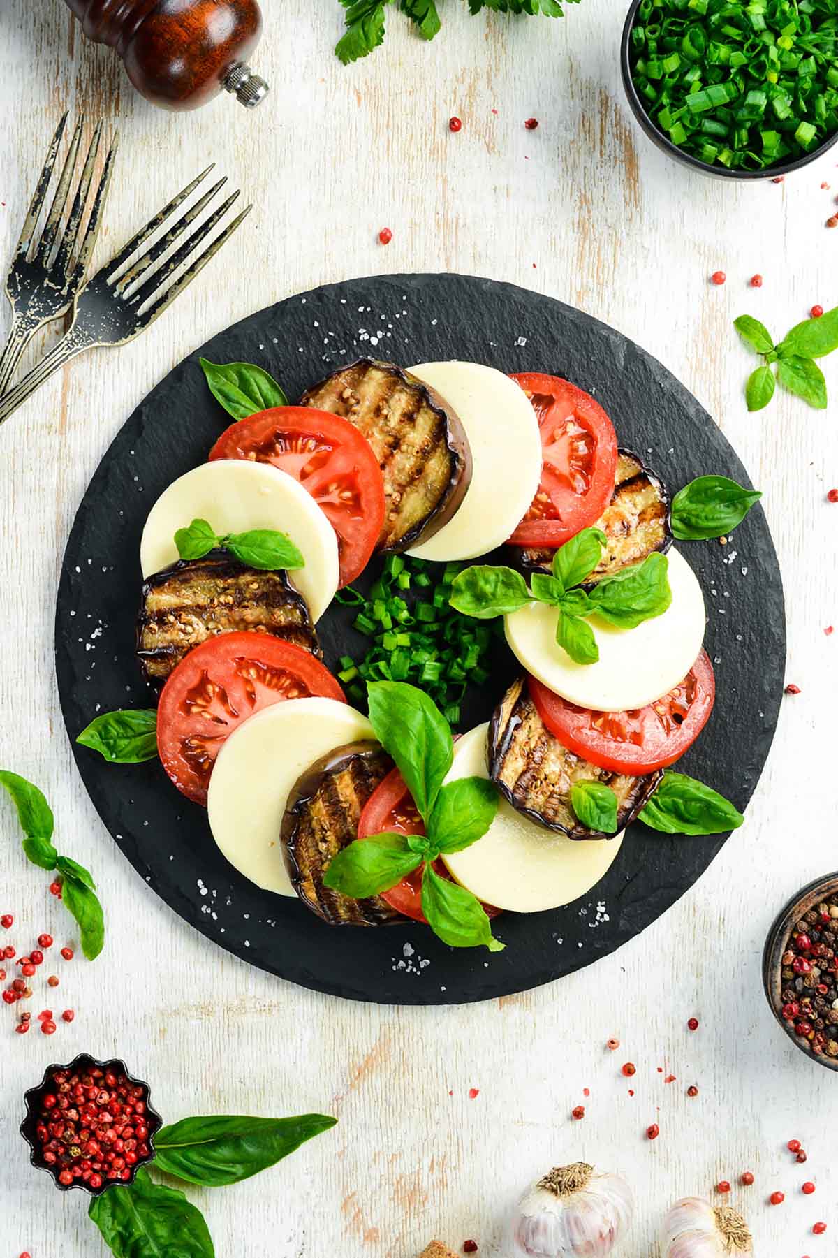 italian caprese salad with grilled eggplant on a black plate.