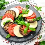 italian caprese salad with grilled eggplant on a black plate.