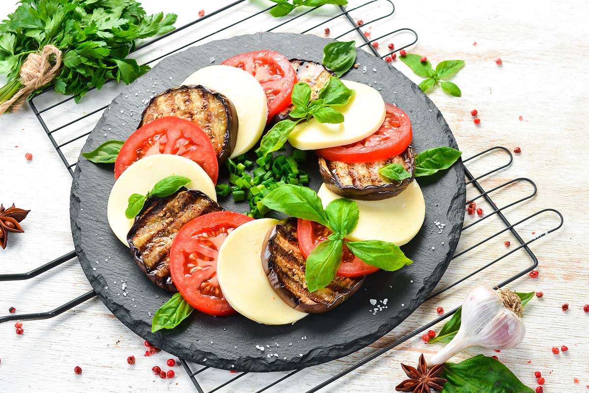 italian caprese salad with grilled eggplant on a black plate.