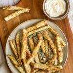 air fried zucchini fries on a plate next to a dip bowl.