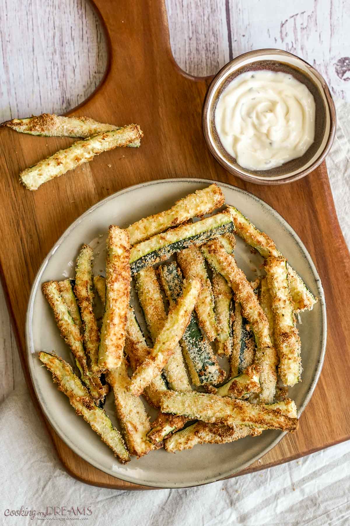 air fried zucchini fries on a plate next to a dip bowl.