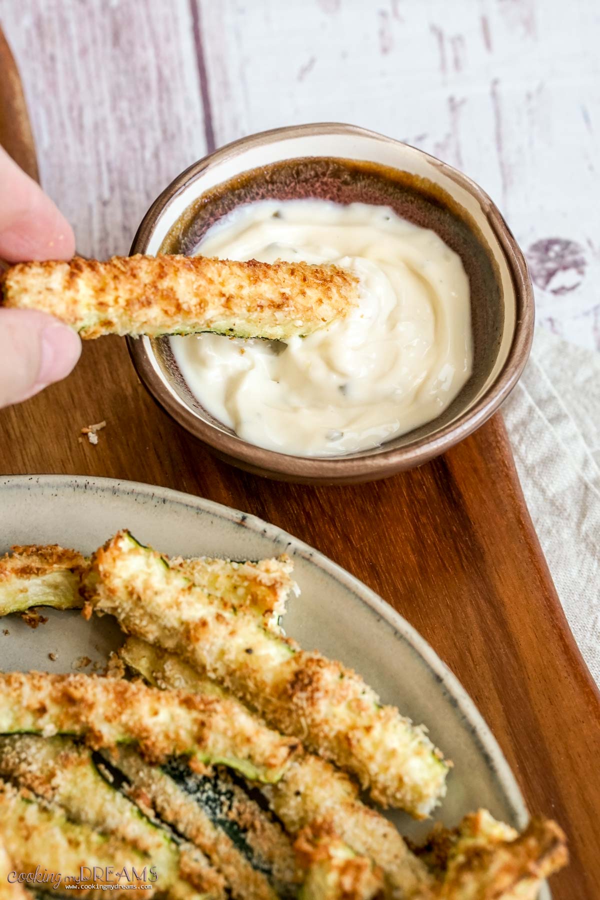hand dipping a zucchini fry into a dip bowl.