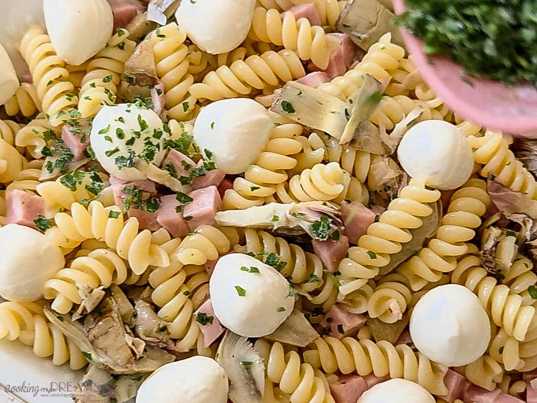 pasta salad is topped with mozzarella balls and parsley.