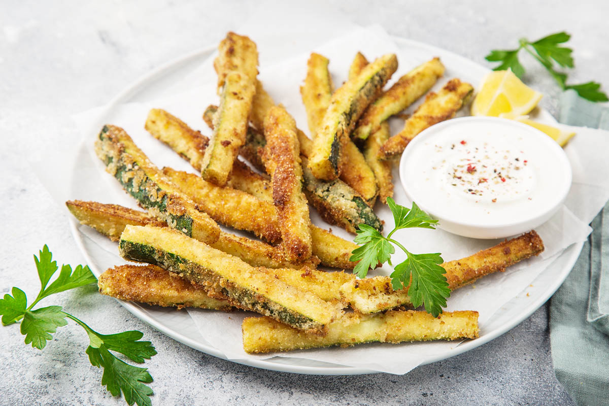 air fryer zucchini fries on a plate next to dipping sauce.