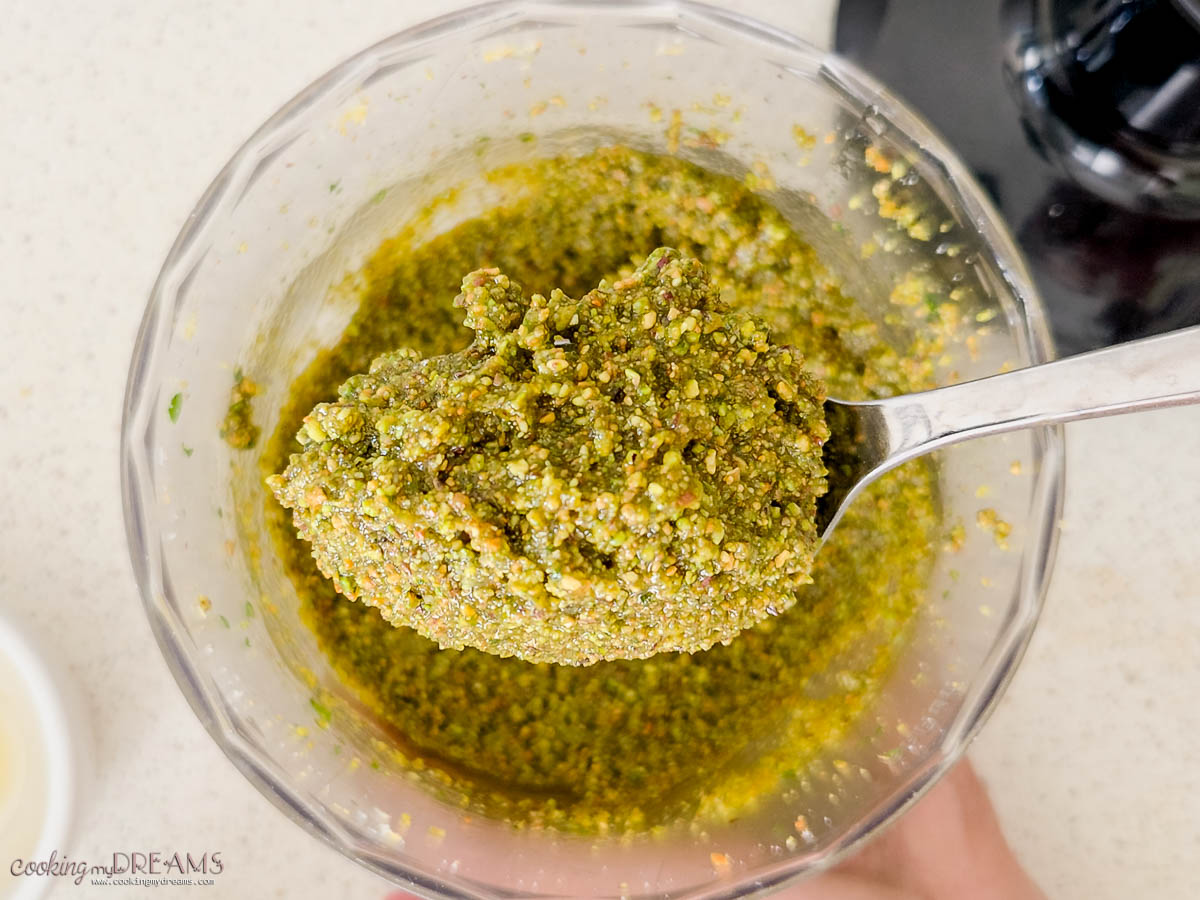 spoon scooping up pistachio pesto from the food processor.