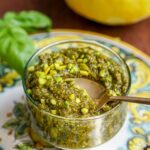 spoon scooping up some pistachio pesto from a glass jar.