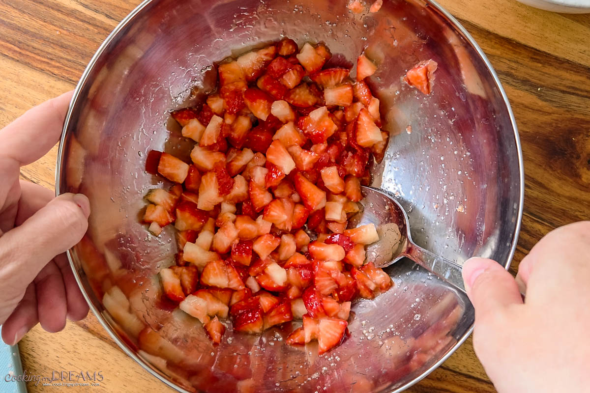 hand mixing chopped strawberries with a spoon.
