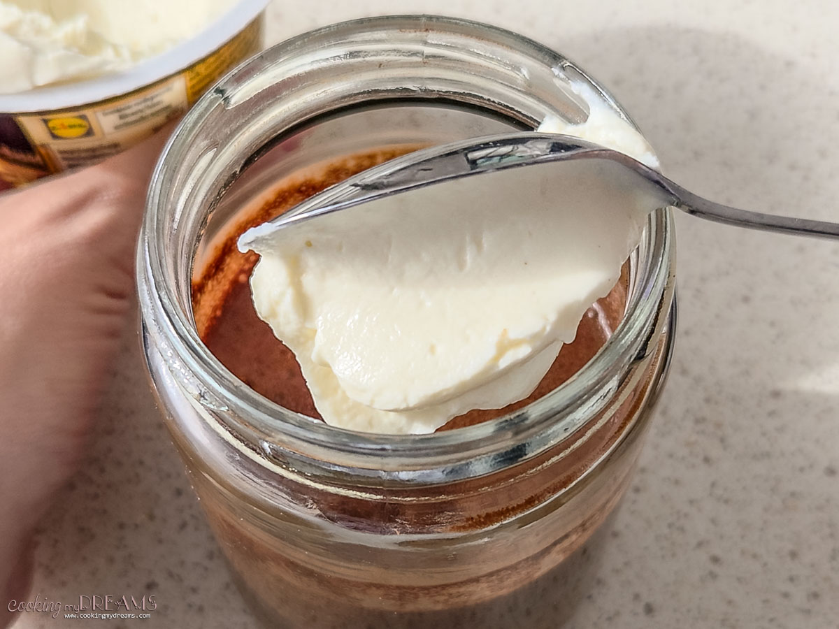 spooning yogurt on top of the oats in the jar.