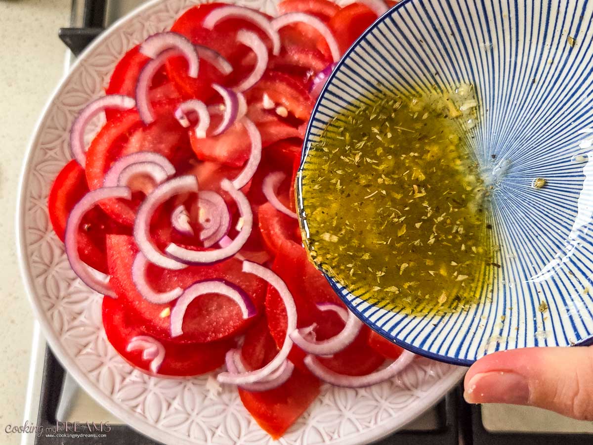 bowl with dressing pouring over the tomato salad.