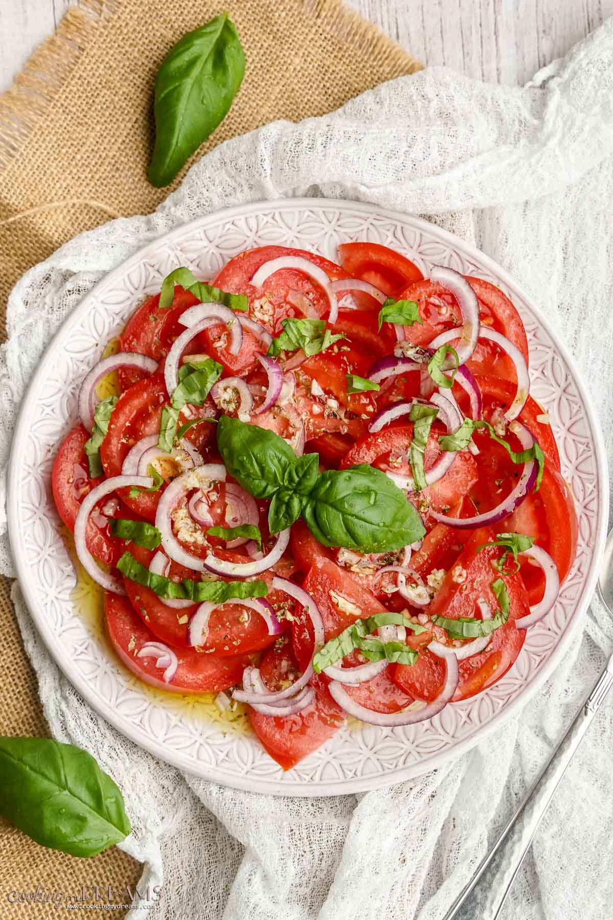 tomato onion salad on a plate topped with basil.