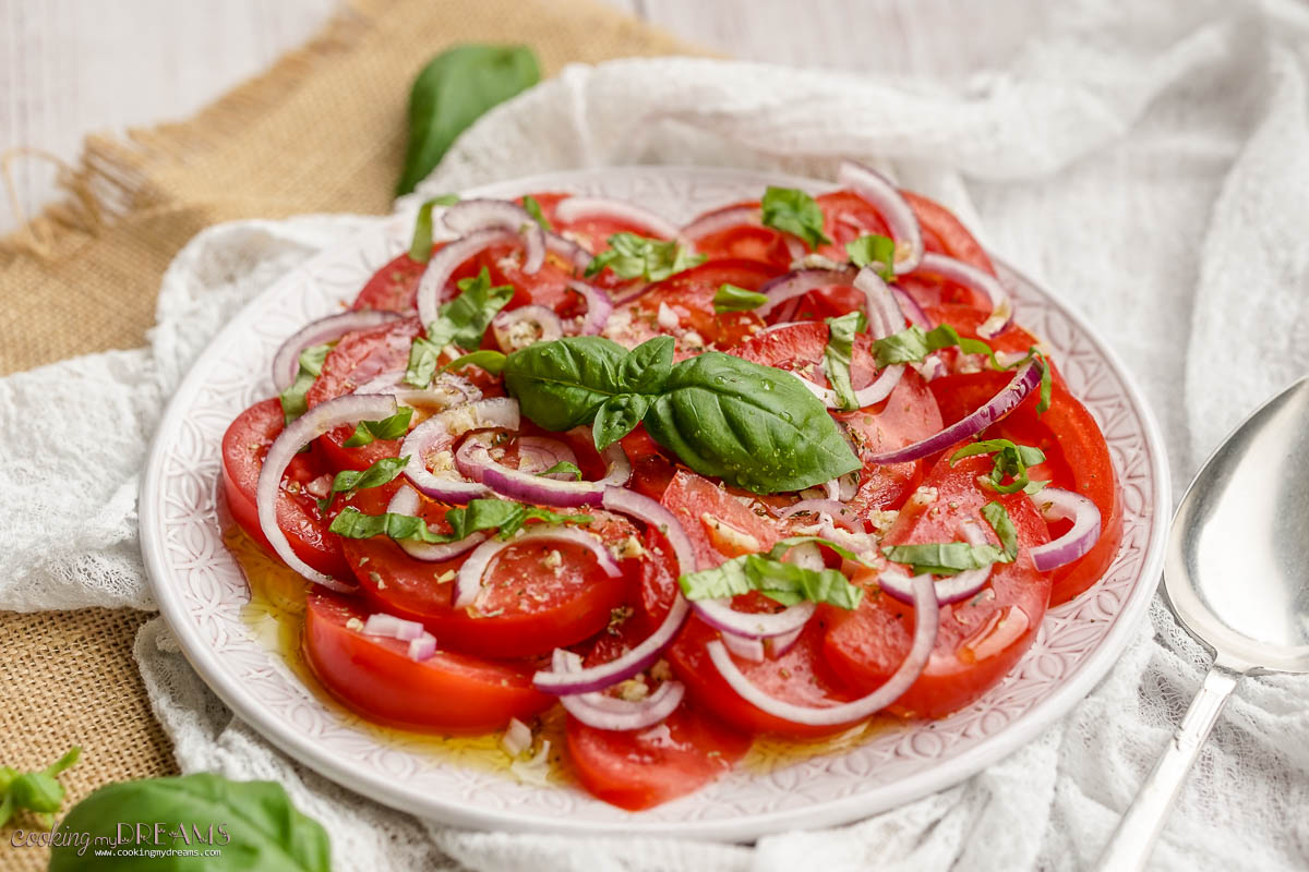 tomato onion salad on a plate topped with basil.