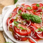 tomato onion salad on a plate with a spoon and topped with basil.