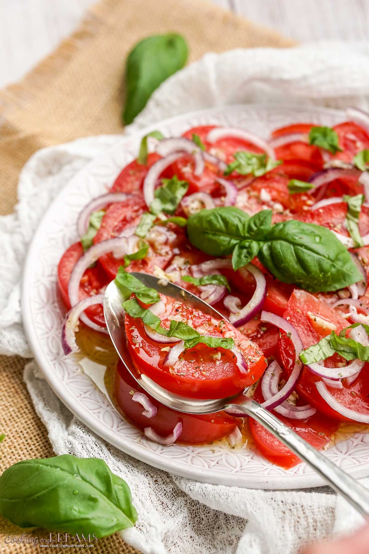 tomato onion salad on a plate with a spoon and topped with basil.
