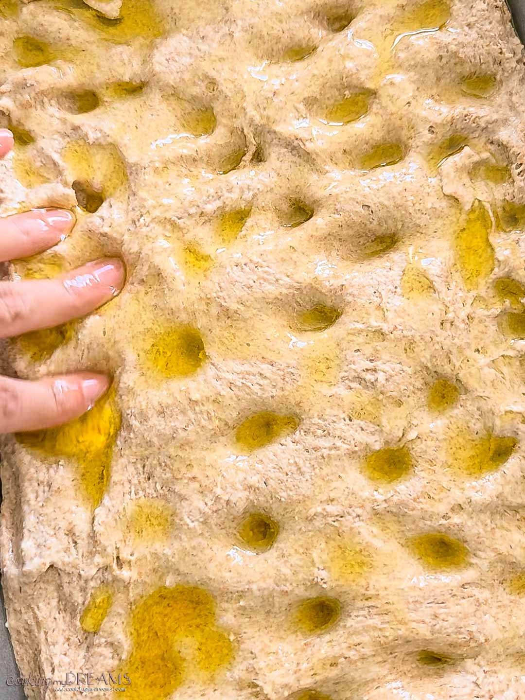 fingers punching holes on a focaccia drizzled with oil.