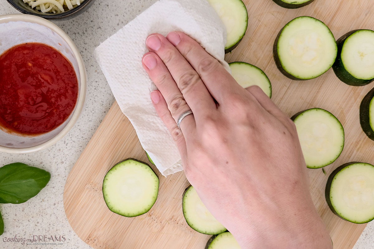 hand patting dry zucchini slices with a paper towel.