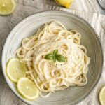 creamy lemon spaghetti in a bowl with lemon slices and basil.