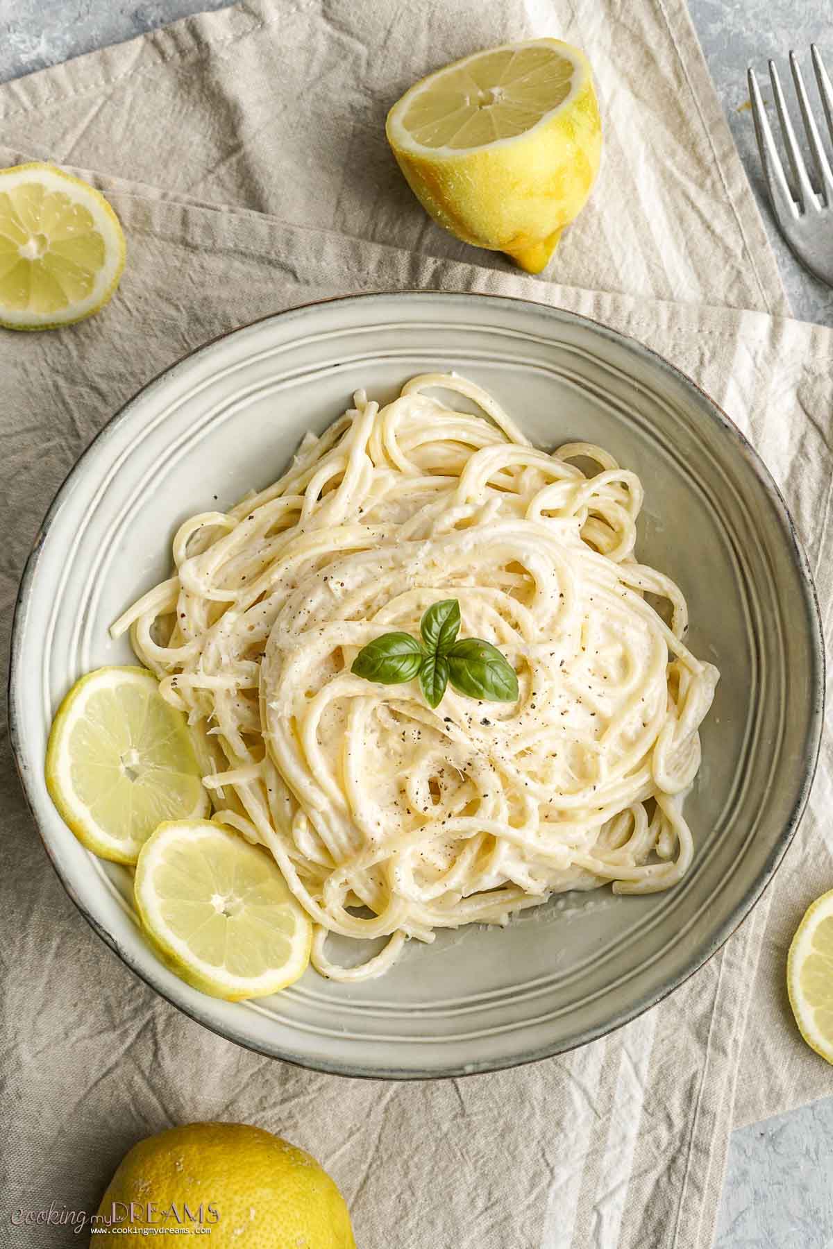 creamy lemon spaghetti in a bowl with lemon slices and basil.